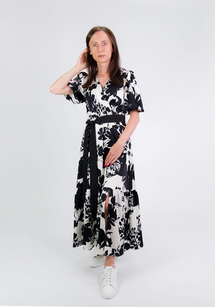 Kobieta ubrana w czarno-białą sukienkę midi Storm Serena Black Flowers w kwiaty z kopertową górą i bufiastymi rękawami, połączona z białymi tenisówkami dla casualowego wyglądu.